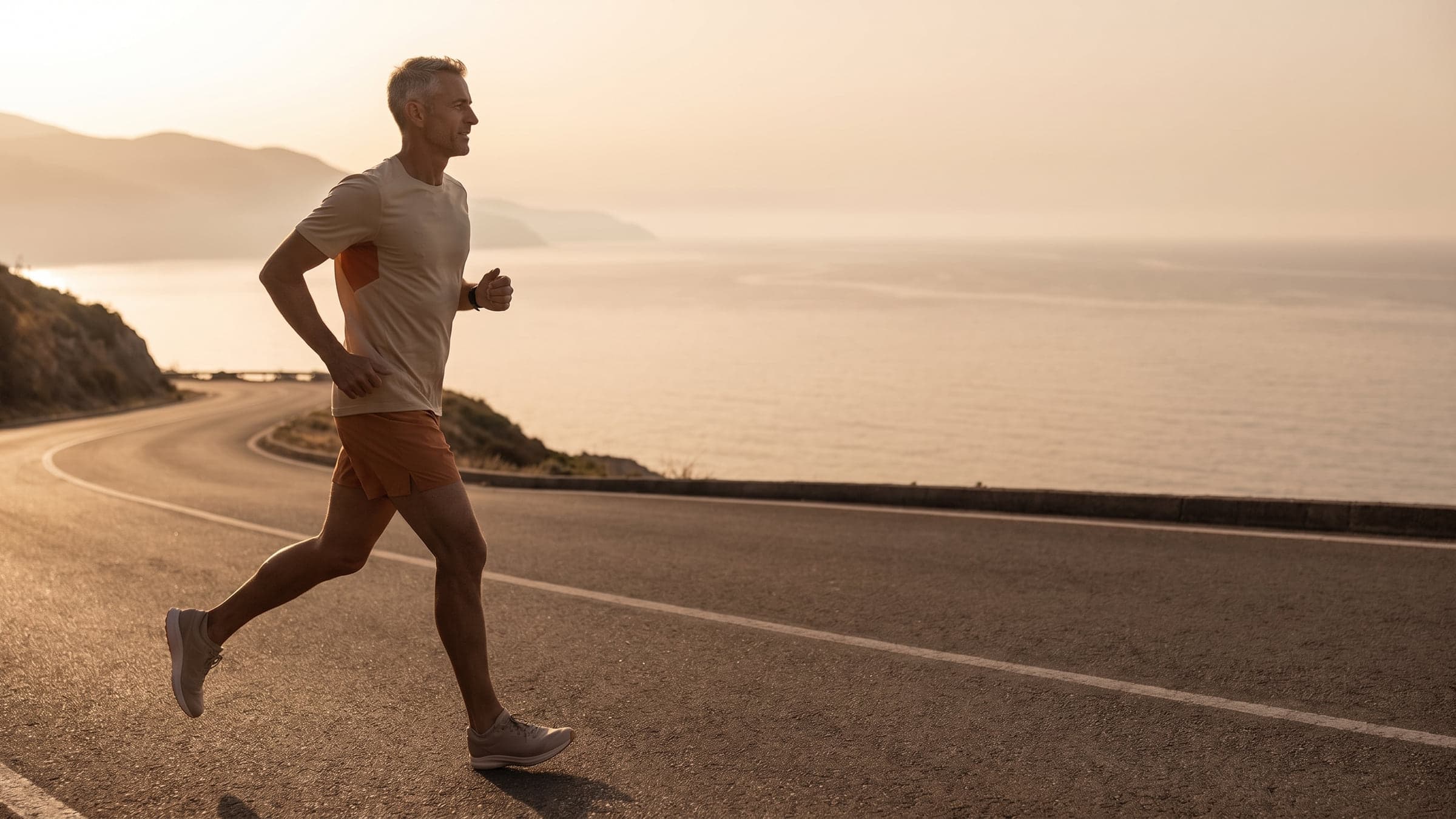 A grey-haired man in his fifties running along a coastal road at sunrise
