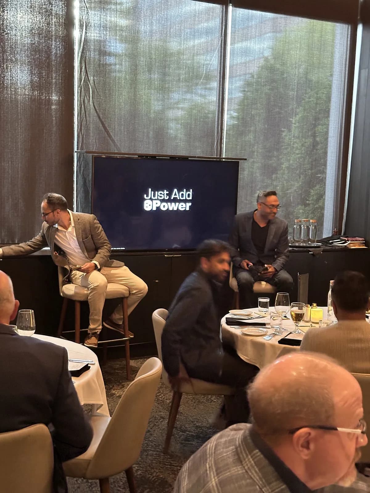 Two speakers taking their stools beside the screen at the front of the room