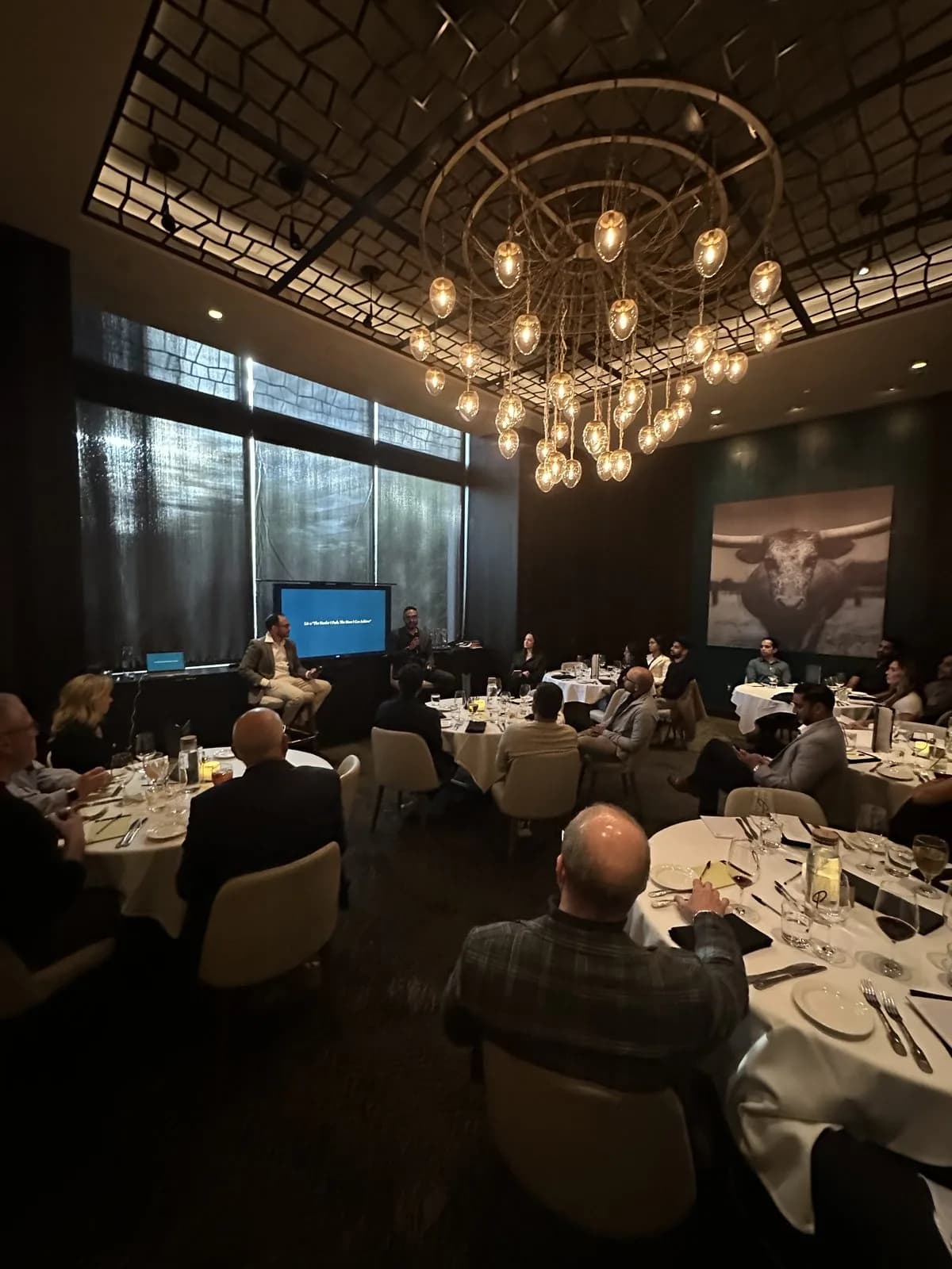 The full room during the talk, the chandelier lit above white linen tables