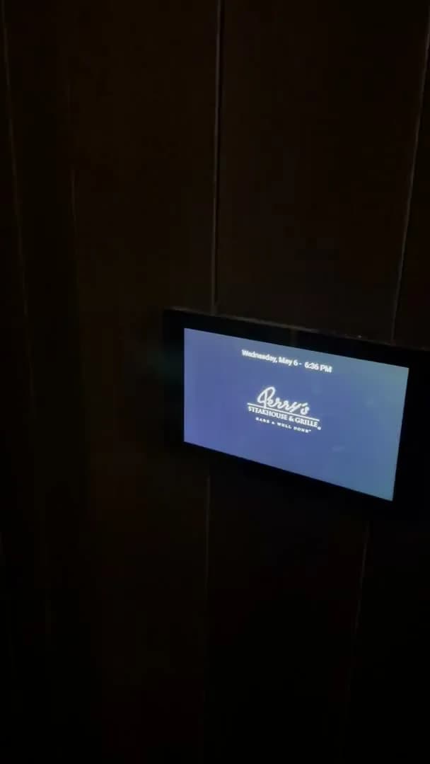 A wall mounted display in the dark corridor outside the private dining room, showing the day and the time