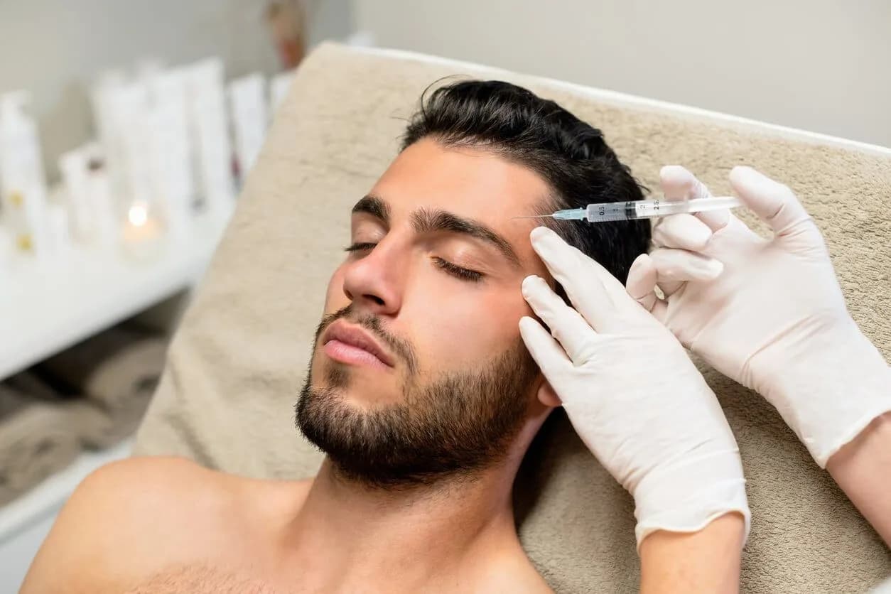 A man reclined on a treatment couch receiving a facial injection from gloved hands