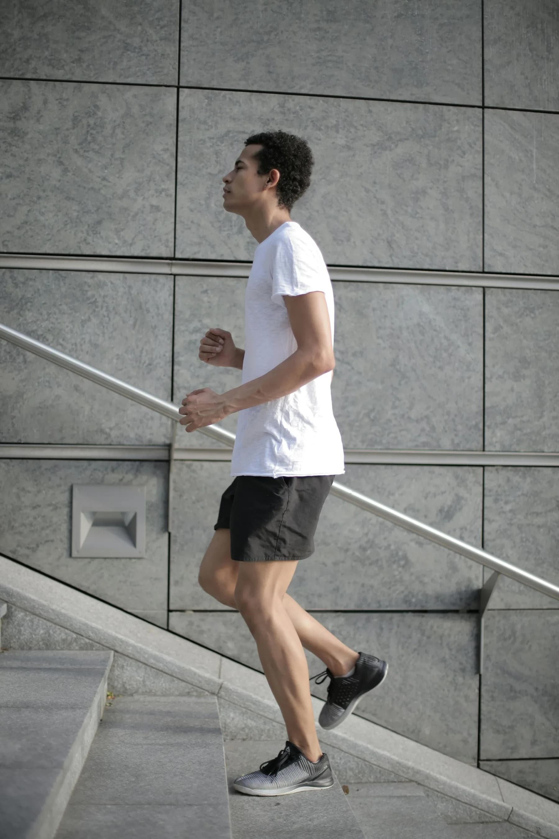 A runner in a white t-shirt climbing a flight of concrete steps beside a grey stone wall