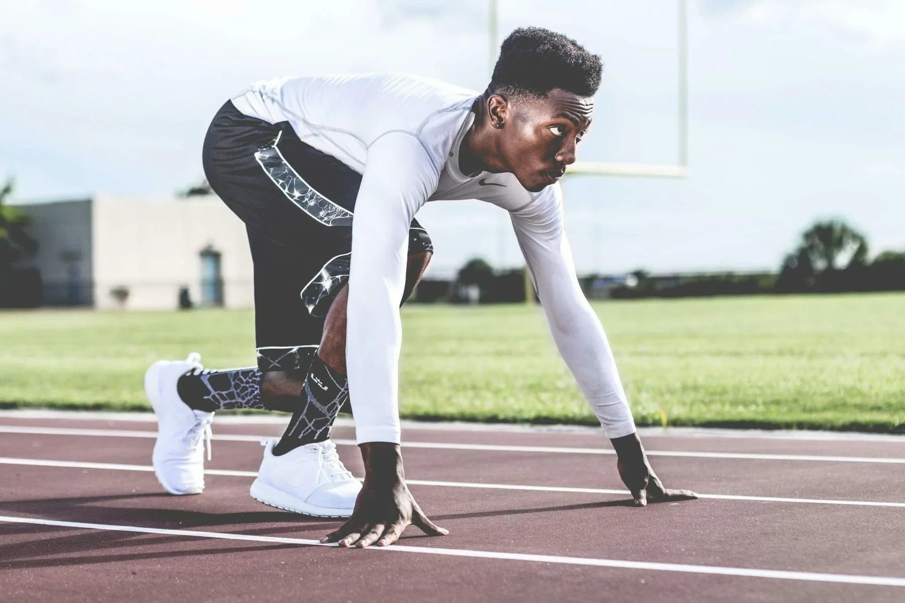 An athlete crouched at the start line of an outdoor running track, hands down, in the moment before a sprint